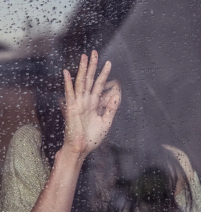 Hand einer trauernden Frau an einer Fensterscheibe mit Regentropfen